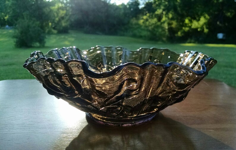 May include: A large, clear glass bowl with a ruffled edge and a textured, floral design. The bowl is made of iridescent glass and has a dark purple hue.
