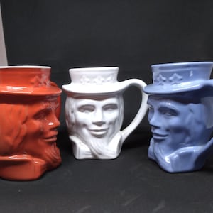 May include: Three ceramic mugs with Uncle Sam faces. The mugs are red, white, and blue.