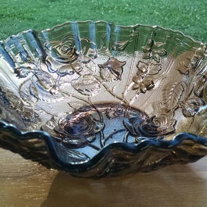 May include: A large, amber-colored glass bowl with a scalloped edge and a floral design. The bowl is made of clear glass with a frosted finish and features a raised design of roses and leaves.