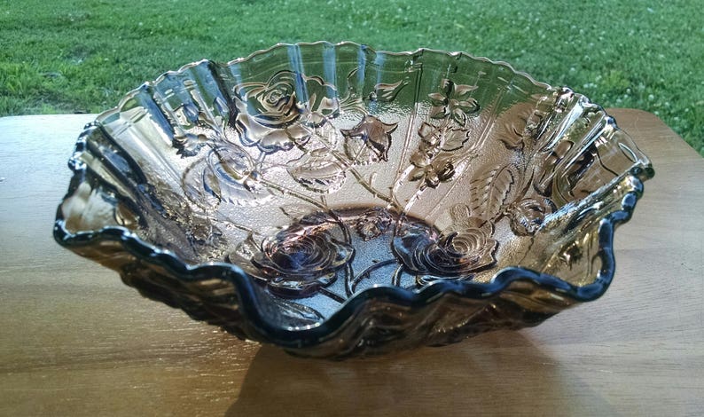 May include: A large, amber-colored glass bowl with a scalloped edge and a floral design. The bowl is made of clear glass with a frosted finish and features a raised design of roses and leaves.