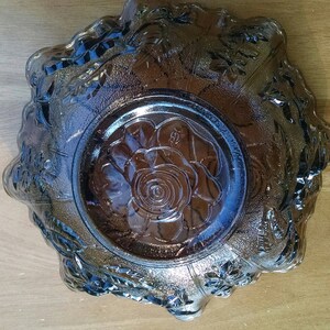 May include: A clear glass bowl with a floral design. The bowl has a raised rim and a center design of a rose. The bowl is a vintage piece and has a frosted look.