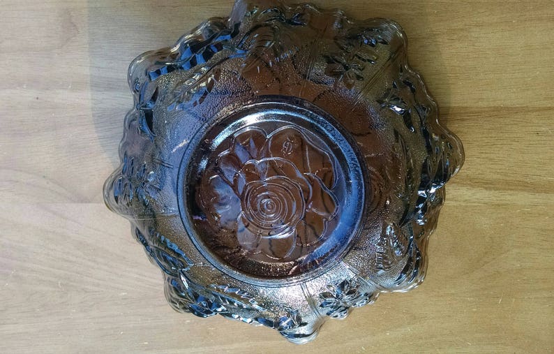May include: A clear glass bowl with a floral design. The bowl has a raised rim and a center design of a rose. The bowl is a vintage piece and has a frosted look.
