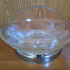 May include: A clear glass serving bowl with a silver metal handle and base. The bowl is divided into three sections and has a decorative, radial pattern.