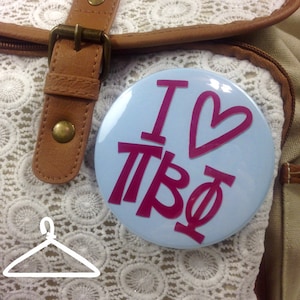 May include: A blue button with a white background and the text "I love Pi Beta Phi" in pink. The button has a heart shape in the middle.