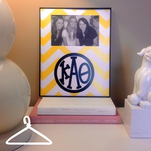 May include: A black and white photo of four women in a yellow and white chevron picture frame with a black circle containing the letters "KAΘ" in white.