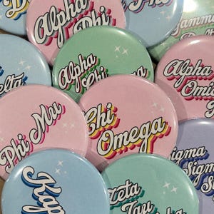 May include: A collection of colorful round buttons with sorority Greek letters in a retro font. The buttons are in shades of pink, blue, green, and lavender. Some buttons have a star design.