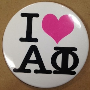 May include: White button with black text that reads "I love A". A pink heart is between the "I" and the "A".