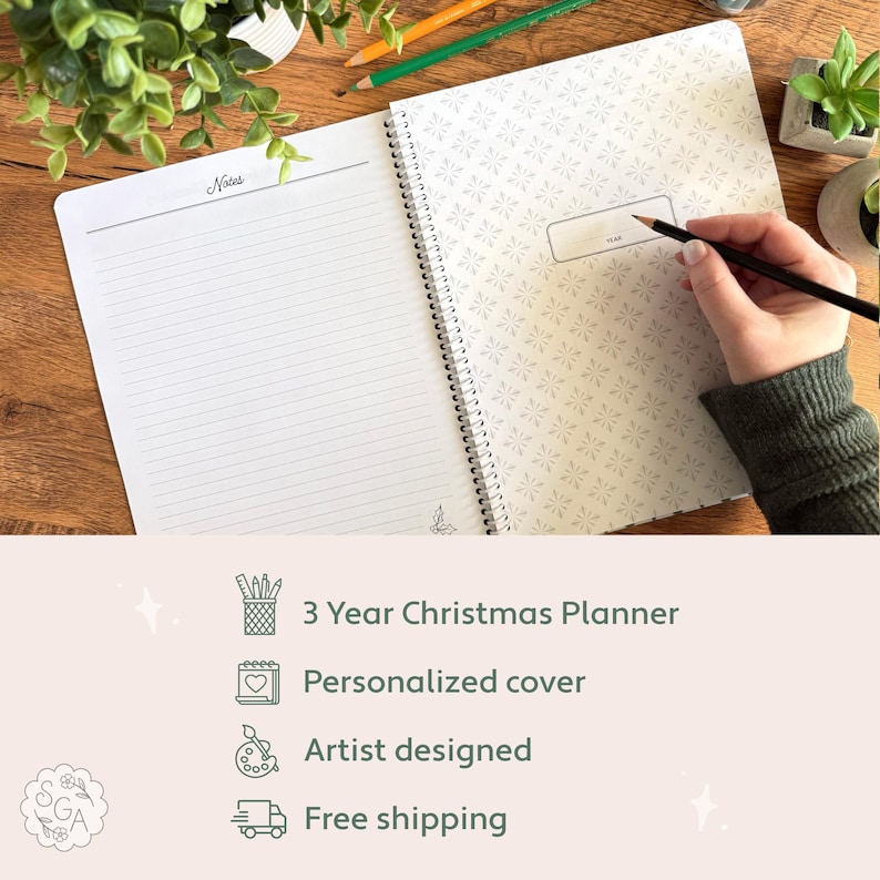 Open personalized Christmas Planning Journal flat lay showing decorative divider page with space to write the year and a Notes page beside it. Hand holding pencil ready to write the year in the planner. Text below highlights 3-year Christmas Planner, personalized cover, artist-designed layout, and free shipping.