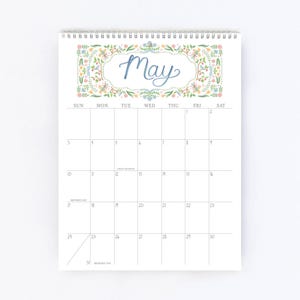 Pu&ograve; includere: Un calendario a spirale per il mese di maggio. La parte superiore presenta la parola &laquo;May&raquo; in corsivo blu, incorniciata da un bordo floreale con accenti verdi, gialli e rosa. La griglia del calendario &egrave; bianca con numeri neri.
