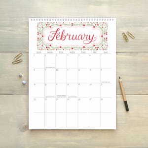 Pu&ograve; includere: Calendario di febbraio con bordo floreale e nome del mese in corsivo. Il calendario &egrave; rilegato a spirale e si trova su una superficie in legno chiaro, con graffette e una matita. Misure in cm.