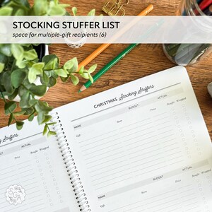 Open personalized 3 Year Christmas Planner flat lay showing “Stocking Stuffers” planning pages. Includes sections for recipient name, budget and actual totals, and checklist to track gifts, stores, prices, and wrapped status. Holiday budgeting and gift organizer notebook for planning Christmas stockings and keeping track of presents and expenses.