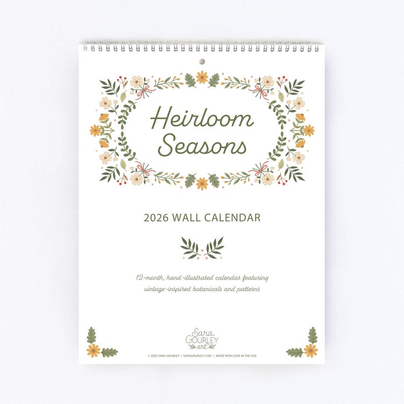 Pu&ograve; includere: Un calendario da parete 2026 con un design floreale. Il calendario presenta il testo "Heirloom Seasons" in una cornice ovale decorativa. La parte inferiore del calendario recita "Calendario illustrato a mano di 12 mesi con botaniche e motivi di ispirazione vintage."