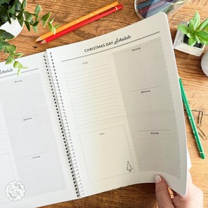 Open Christmas Planner Book showing “Christmas Day Schedule” page with sections for morning, afternoon, evening, to-do list, and notes. Hand turning the page to reveal the next section of the planner. Holiday organization notebook for Christmas day planning, time management, and festive to-dos.