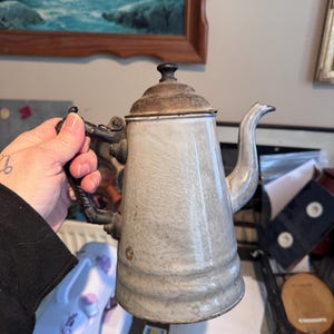 May include: A white ceramic mug with a black handle and the text "But First, Coffee" in a black, handwritten-style font. The mug is on a white surface.