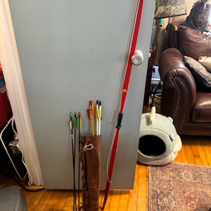 May include: A red wooden bow and arrow set with a brown leather quiver and colorful arrows.