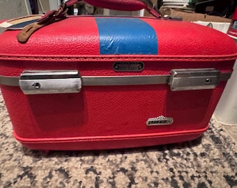 American Tourister Tiara red train case from the 1960s, featuring a bright red hard shell and a bold blue stripe with yellow bakelite tray