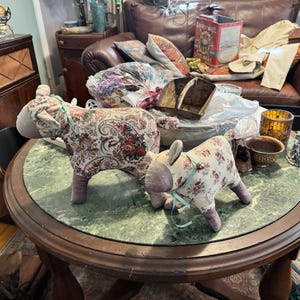 May include: Two fabric covered animal figurines, one with a floral pattern and the other with a paisley pattern, are sitting on a round green marble table with a wooden frame.