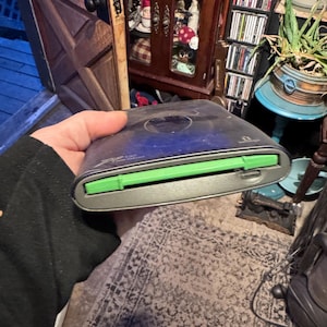 May include: A dark blue and grey external Zip 100 drive featuring a bright green eject button and a horizontal disk insertion slot. The device has a rounded rectangular shape with the text Zip 100 printed in white on the top surface.