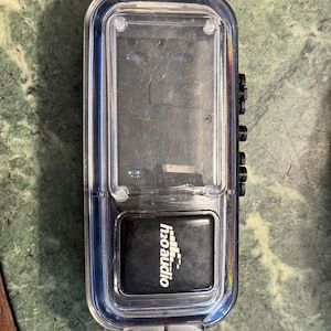 May include: A clear plastic waterproof case with a black h2o audio logo on the front. The case has a black rubber seal around the edges.