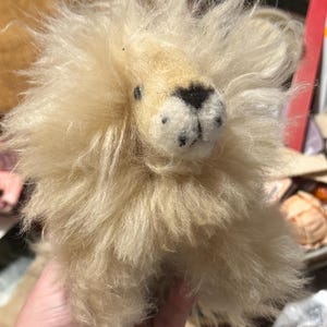 May include: A small, cream-colored stuffed lion with a fluffy mane. The lion has black eyes and a black nose.