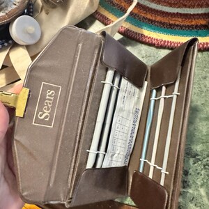 May include: A brown Sears crochet hook and needle case, open to reveal crochet hooks and knitting needles. The case has a gold clasp and the Sears logo. A chart with measurements is visible.