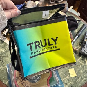 May include: A rectangular, insulated cooler bag with a gradient design of blue and yellow. The bag features the text "TRULY HARD SELTZER" in black. The bag is open, revealing a green interior.