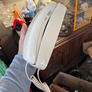 May include: A white corded telephone handset with a coiled cord. The handset features a small sliding switch on the side with the text "NORMAL" and "LOUD" printed next to it, indicating volume settings for the device's audio output.