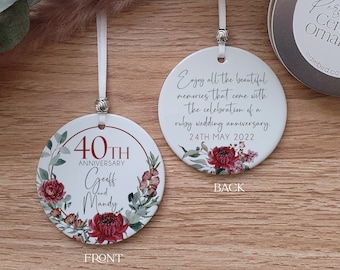 Pode incluir: Um ornamento de cerâmica branca com um design floral e o texto "40th Anniversary Geoff and Mandy" na frente. A parte de trás do ornamento tem o texto "Enjoy all the beautiful memories that come with the celebration of a ruby wedding anniversary. 24th May 2022".
