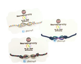May include: Three infinity symbol bracelets on display. Each bracelet features a colorful cord and a metal infinity symbol. The cards read "Neurodiversity" and "We all think differently" with a social media handle.