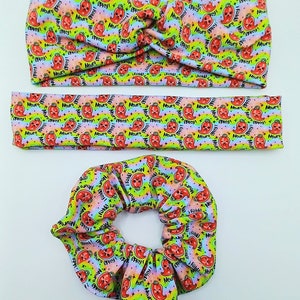 May include: A set of three hair accessories featuring a colorful rainbow pattern with red chili peppers and the text "I fold a mean spicy" repeated throughout. The set includes a headband, a scrunchie, and a skinny headband.