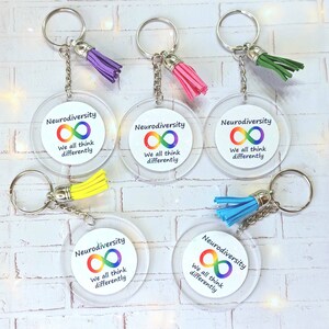 May include: Five clear acrylic keyrings with rainbow infinity symbols and the text "Neurodiversity We all think differently". Each keyring has a different coloured tassel: purple, pink, green, yellow, and blue.