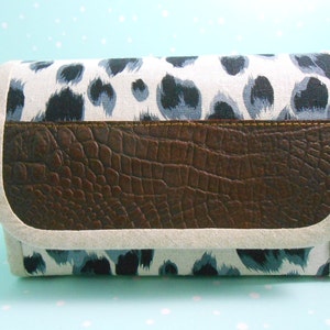 May include: A rectangular clutch bag featuring a brown faux-crocodile leather flap and a white fabric body patterned with blue and black spots. The edges are trimmed with a light beige fabric.