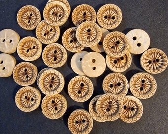 May include: A collection of 25 round wooden buttons with a floral design. The buttons are a light brown color with a darker brown floral pattern.