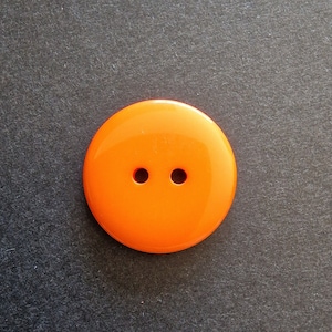 Könnte beinhalten: Ein knallorangefarbener Plastikknopf mit zwei Löchern.