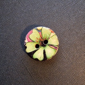 Könnte beinhalten: Ein zweilöchriger Holz-Knopf mit einem grünen, rosa und schwarzen Blumendesign.