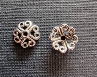Pode incluir: Duas tampas de contas de metal prateado com um design floral decorativo e intrincado. As tampas têm um pequeno furo no centro para enfiar.