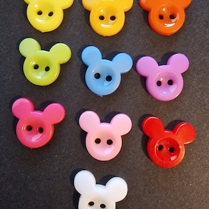 Könnte beinhalten: Zwölf Plastikknöpfe in Form von Mickey-Maus-Köpfen in verschiedenen Farben, darunter Gelb, Grün, Blau, Rosa, Rot und Weiß.