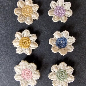 Peut inclure: Six appliqués de fleurs au crochet faites à la main. Chaque fleur a un motif de pétales blancs avec un centre de couleur différente : jaune, violet, bleu, rose et vert. Ces petites décorations florales sont idéales pour l'artisanat.