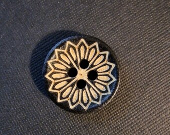 May include: A black wooden button with a white floral design and three holes.