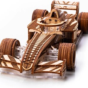 Peut inclure: Maquette en bois d'une voiture de course de Formule 1. Le modèle est fait de bois brun clair et foncé, avec des détails complexes. Les roues sont épaisses et arrondies. La voiture est posée sur un socle en acrylique transparent.