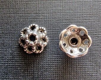 Pode incluir: Duas tampas de contas de metal prateado com um design de flor. Uma tampa tem um design mais intrincado com um centro elevado e detalhes vazados. A outra tampa tem um design mais simples com um centro liso e detalhes vazados.