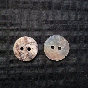 Peut inclure: Deux boutons ronds à deux trous en nacre. Un bouton a un motif marbré brun et blanc, l'autre est brun clair avec un éclat nacré.