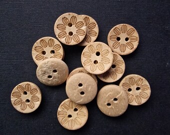May include: A collection of 12 natural wood buttons with a floral design. The buttons are light brown and have two holes each.