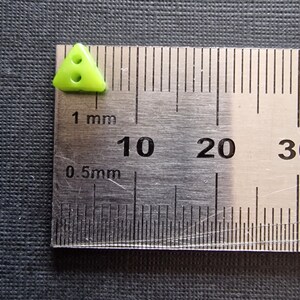 Peut inclure: Un bouton triangulaire de couleur vert lime avec deux trous. Le bouton mesure environ 0,5 cm de large.