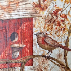 Op de afbeelding: Een bruine vogel met rode accenten zit op een tak voor een rood vogelhuisje met een wit dak. Het vogelhuisje heeft een kleine opening waar vogels naar binnen kunnen. De achtergrond is een aquarel van bruine takken en bladeren.