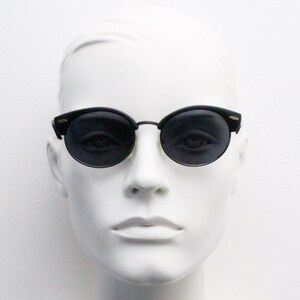 May include: A white mannequin wearing black round sunglasses with a thin gold frame.