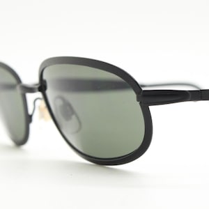 90's vintage black oval sunglasses made in Austria. Minimal matt finish solid metal flat frame with green lenses. Unworn  NOS