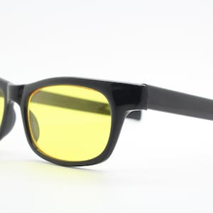 May include: Black framed glasses with yellow lenses. The glasses have a simple, classic design.