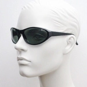 Könnte beinhalten: Schwarze ovale Sonnenbrille mit dunkelgrünen Gläsern. Die Sonnenbrille sitzt auf einem weißen Mannequin-Kopf.