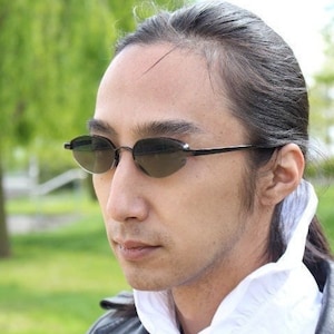 May include: A person wearing black framed sunglasses with a dark lens. The person has long dark hair pulled back and is wearing a white collared shirt and a black leather jacket.